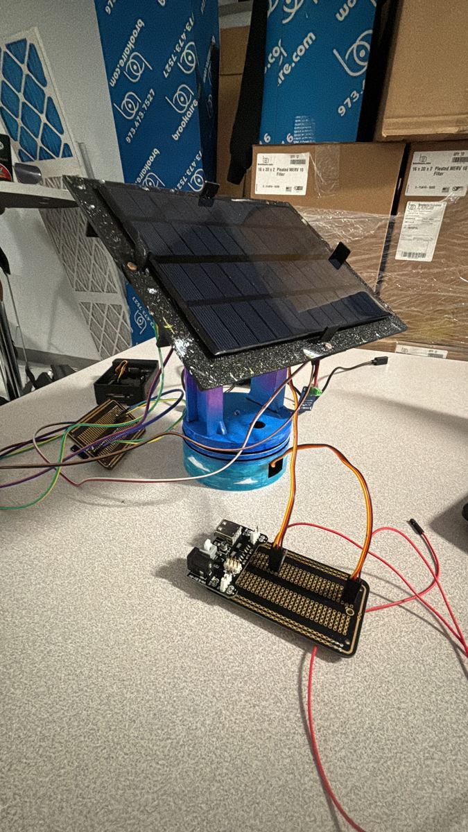 The tracker with a blue base, solar panel on top and loose jumper wires on the table
